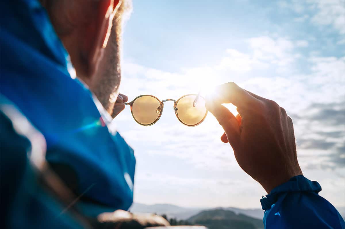 A man checking his sunglasses lenses by holding them up to the sun