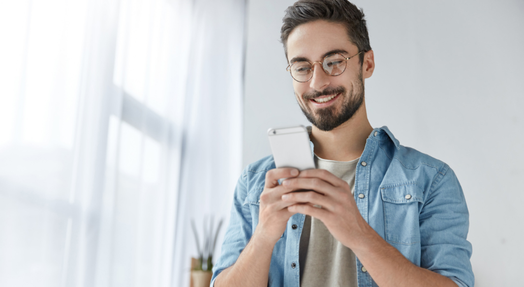 Cheerful man with beard holds modern smart phone and wearing glasses