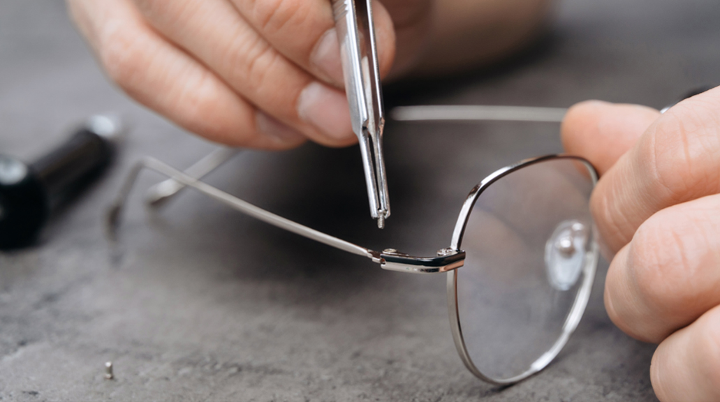 Closeup of person's hands repairing arm of glasses with special tools and equipment