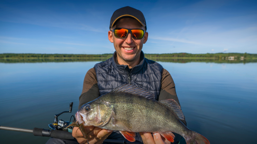 Man smiling wearing sunglasses whilst holding a fish he's caught whilst fishing