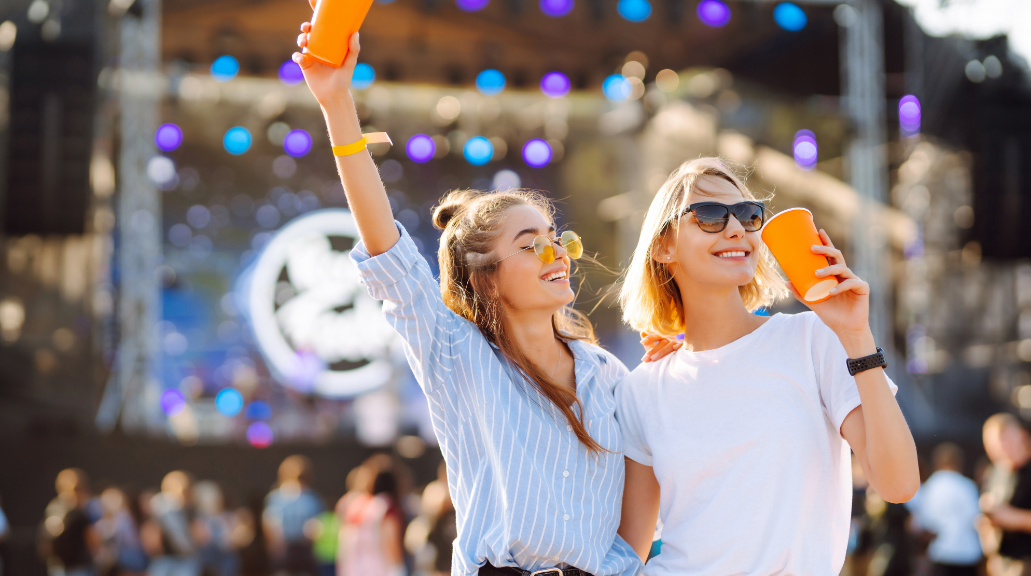 Two young woman wearing sunglasses holding beer at music festival