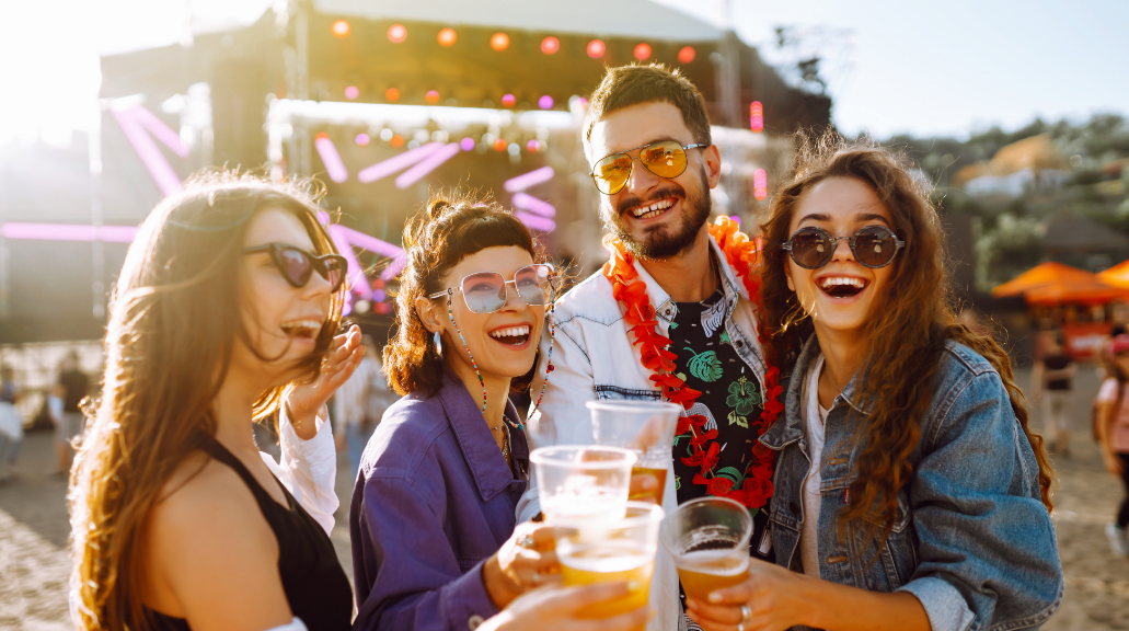 Young happy friends wearing sunglasses drinking beer and having fun at music festival together