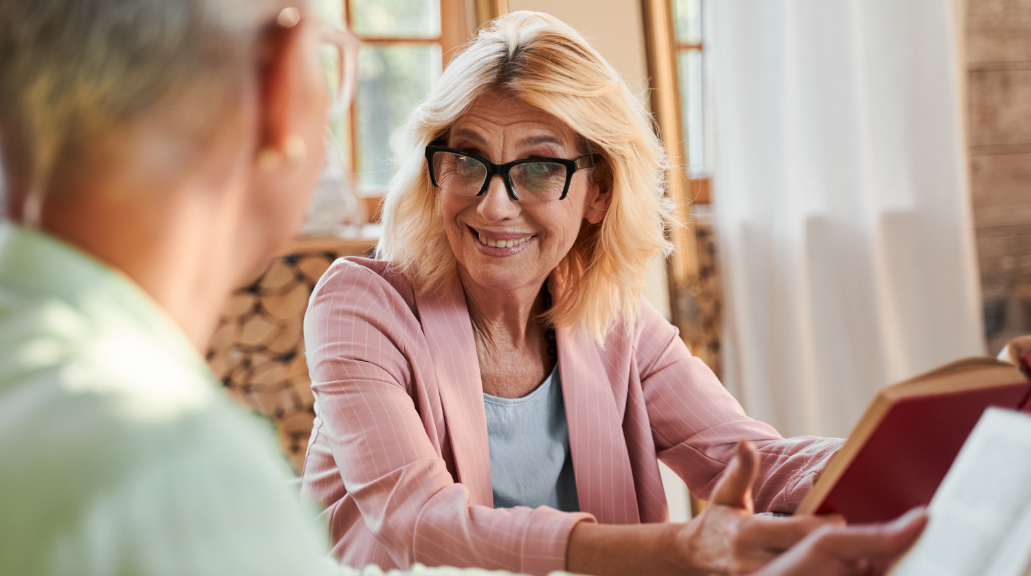 Mature woman wearing glasses smiling whilst holding a book