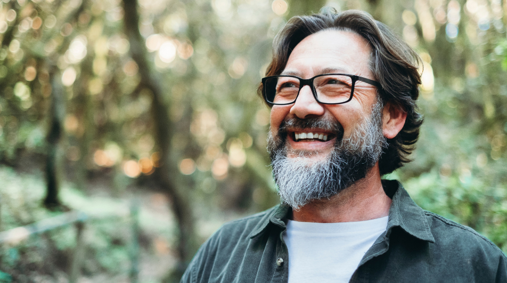 Mature man smiling wearing glasses whilst walking through woods