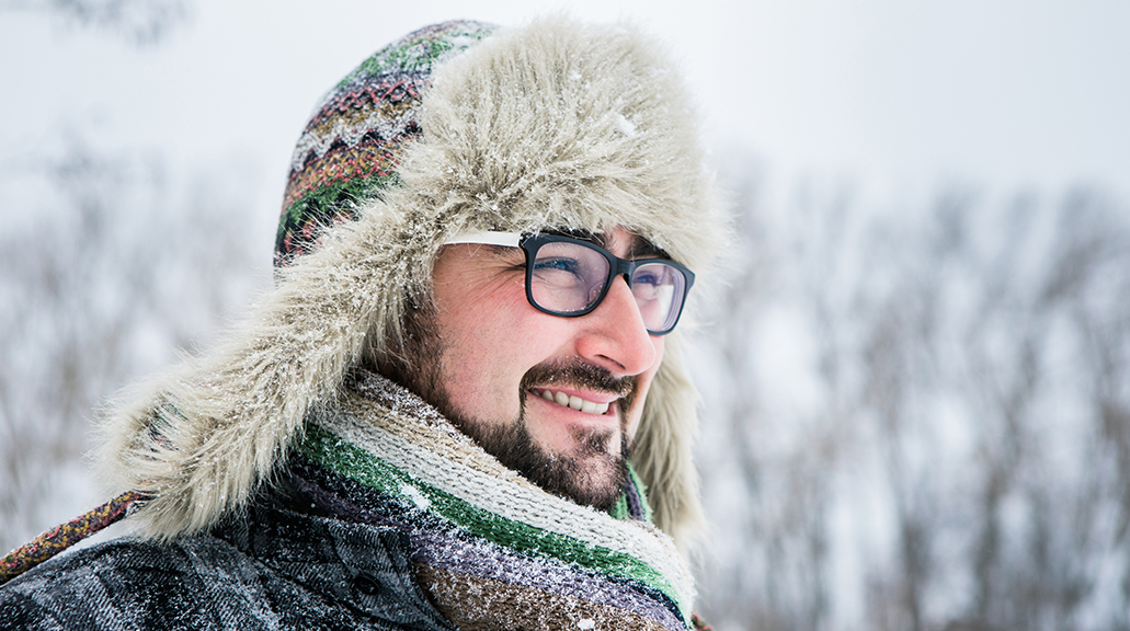 Happy man walking in the snow wearing glasses smiling at the camera