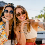 Stylish smiling women relaxing having fun at the beach wearing sunglasses, using smartphone to take selfie picture