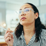 Business woman wearing glasses, holding pen thinking