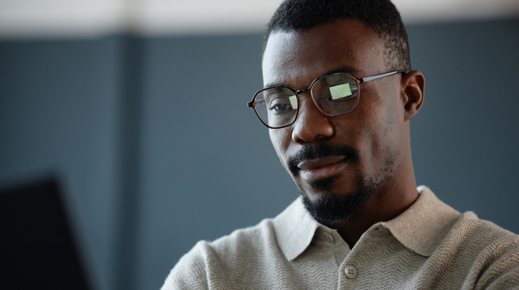 Portrait of man wearing glasses working on laptop with relaxed facial expression at office workplace