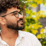 Portrait of a young man wearing glasses, smiling and looking away in a garden with a blurred background