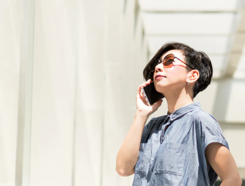 Stylish woman talking on mobile phone outside a building on a sunny day. She's wearing reactolite lenses